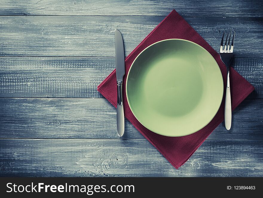 Plate, knife and fork at napkin on wooden background