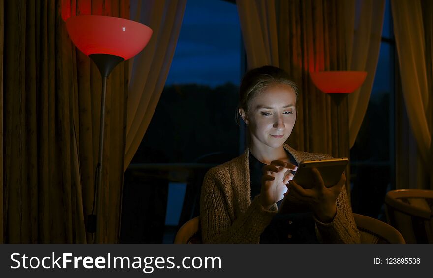 Woman using digital tablet computer device in cafe of cruise ship. Evening time, lowlight. Technology and entertainment concept