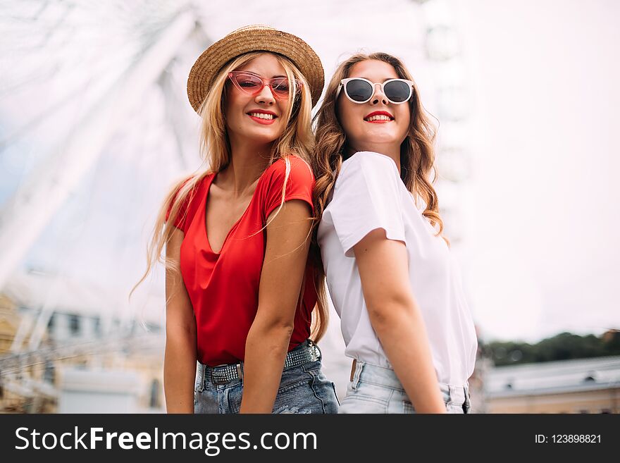 Closeup portrait happy smiling pretty girls having fun.stylishly dressed in short denim shorts and bright t-shirts, sunglasses.posing on the background of a ferris wheel