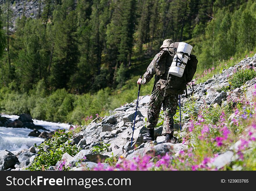 A Man With A Backpack Walks Along A Mountain River.