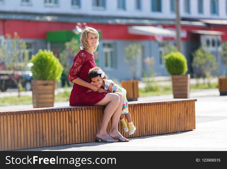 Caucasian Woman With Black Girl Sitting On A Bench.