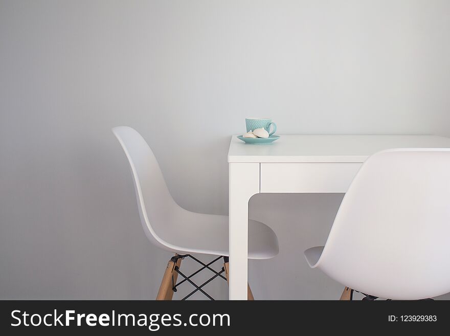 Turquoise cup of tea and meringue on a white table near white chairs.