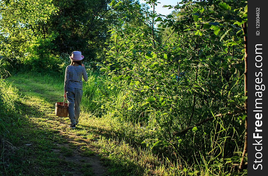 Young girl walking on a path through green woods carrying a basket