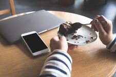 A White Mobile Phone With Blank Black Desktop Screen Next To Laptop With A Woman Eating Brownie Cake Royalty Free Stock Photos