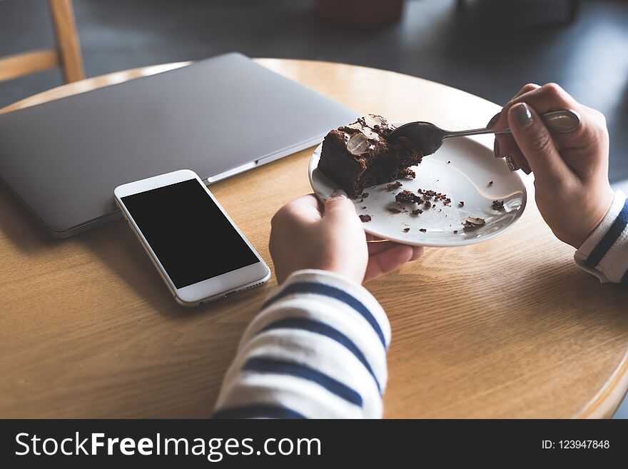 A white mobile phone with blank black desktop screen next to laptop with a woman eating brownie cake