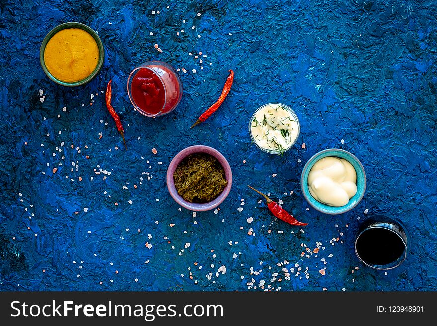 Set of sauces. Ketchup, mayonnaise, mustard, soy sauce, barbecue sauce, pesto, mustard, sour with greenery near chili pepper on blue background top view.