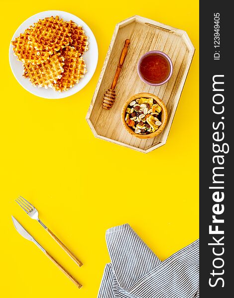 Round belgian waffles for breakfast. Breakfast in bed. Waffles on plate. Honey and dried fruits in tray, knife and fork, tablecloth on yellow background top view.