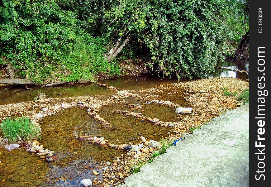 A tropical scene of a freshwater river flowing over big rounded pebbles. It's sad to see some irresponsible people leaving behind they rubbish into this river. A tropical scene of a freshwater river flowing over big rounded pebbles. It's sad to see some irresponsible people leaving behind they rubbish into this river.