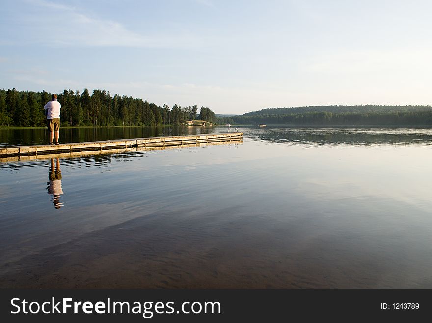 Man standing on a wooden landing stage watching a still lake. Man standing on a wooden landing stage watching a still lake