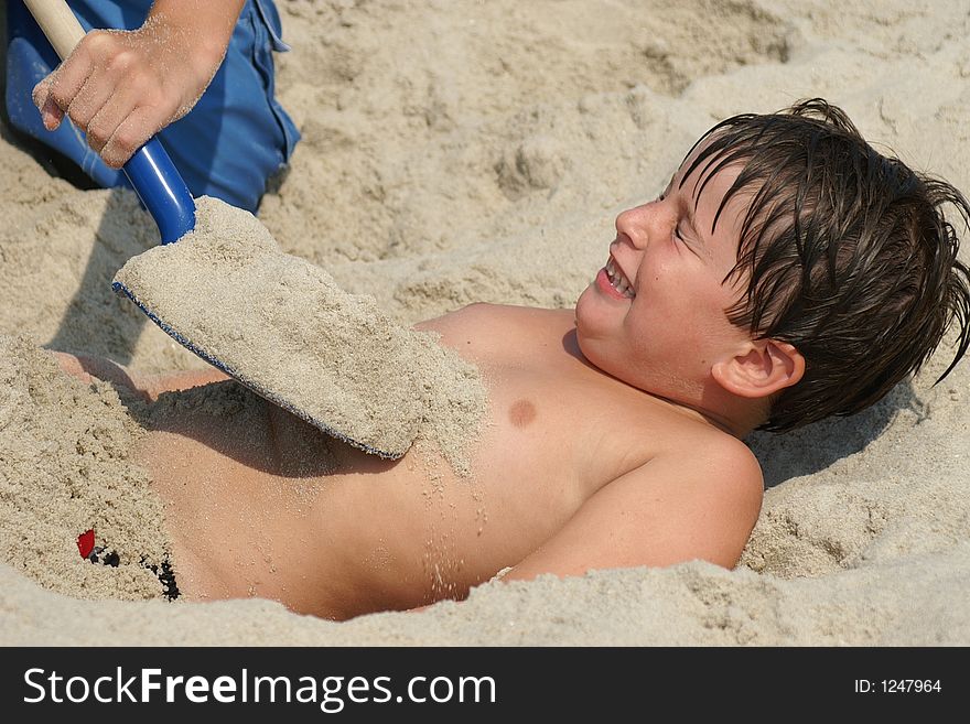 Boy getting buried in the sand on the beach