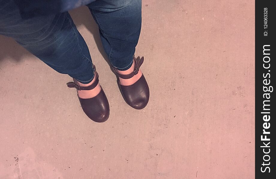 Woman standing on concrete, photo showing her legs and feet. She is wearing blue jeans and brown leather shoes, standing on concrete. Woman standing on concrete, photo showing her legs and feet. She is wearing blue jeans and brown leather shoes, standing on concrete.