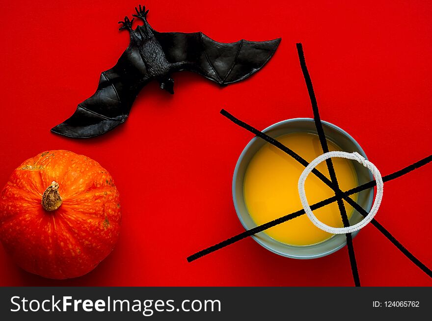 Pumpkin soup in blue bowl isolated on red background, top view. Symbol of HALLOWEEN is black spiderweb and bat , copy space, closeup,