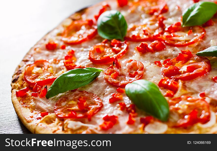 Pizza with Mozzarella cheese, Ham, Tomatoes, pepper, Spices and Fresh Basil. Italian pizza on wooden background.