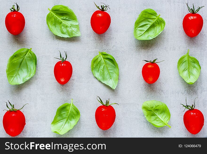 Creative layout made of cherry tomato and basil leaves on light background close up. Ingredients for healthy cooking. Food concept. Flat lay, top view. Creative layout made of cherry tomato and basil leaves on light background close up. Ingredients for healthy cooking. Food concept. Flat lay, top view