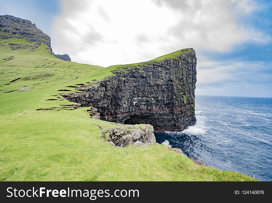 Amazing dramatic view of steep cliff in front of Drangarnir in Vagar island, Faroe Islands, Denmark north Atlantic ocean, best destination for hiking, stunning sea stack with deep blue water.