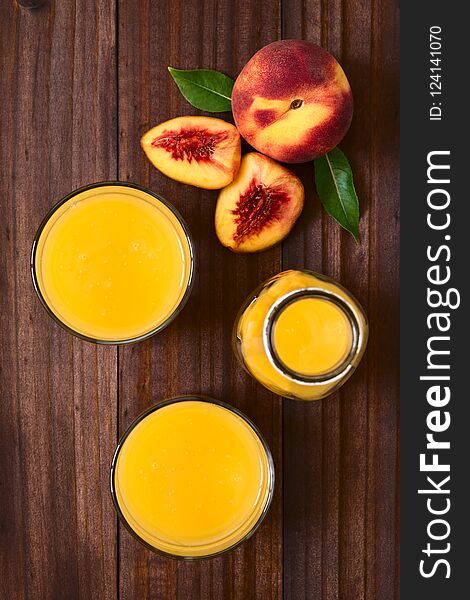 Peach juice or nectar in glasses and in bottle with fresh ripe peach fruits on the side, photographed overhead on dark wood with natural light Selective Focus, Focus on the top of the juices and the top of the whole fruit
