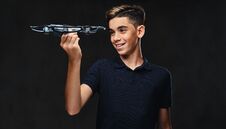 Joyful Young Guy Dressed In A Black T-shirt Holds A Quadcopter. Isolated On The Dark Background. Stock Image Joyful Young Guy Dressed In A Black T-shirt Holds A Quadcopter. Isolated On The Dark Background. Stock Image