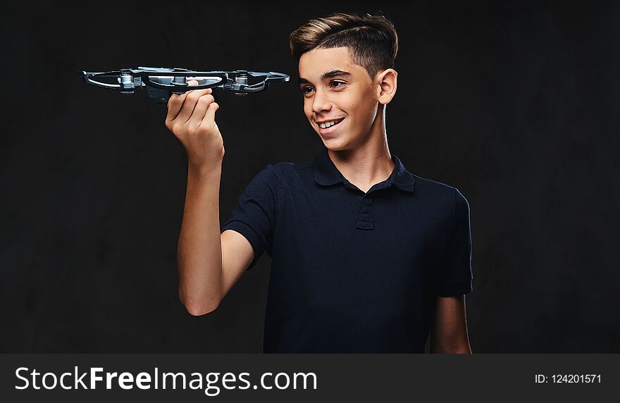 Joyful young guy dressed in a black t-shirt holds a quadcopter. Isolated on the dark background.