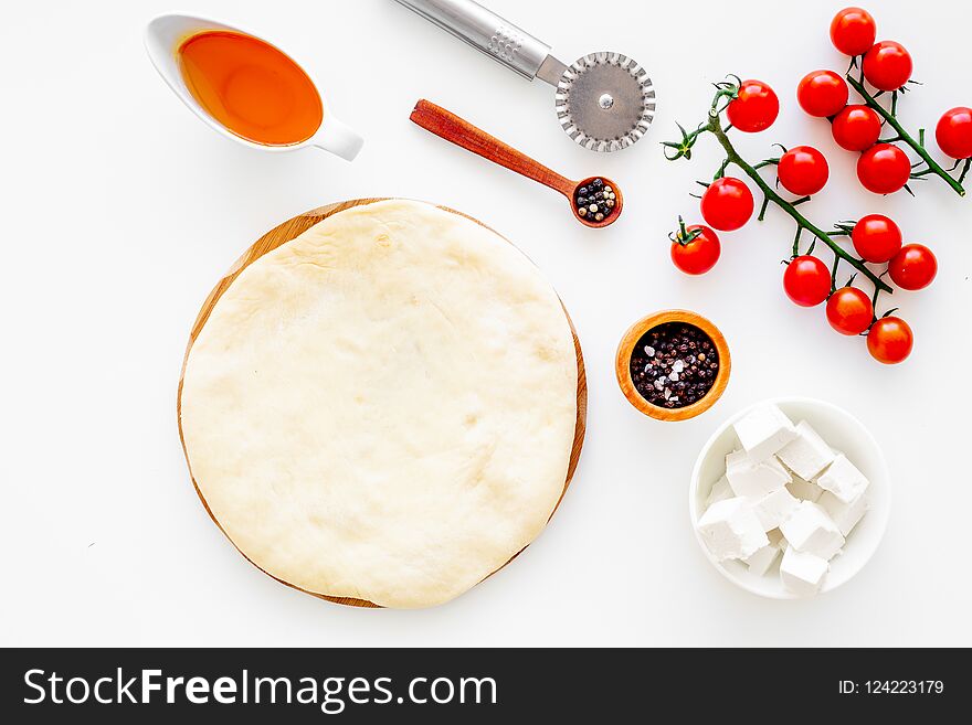 Make pizza concept. Pizza dough and ingredients for filling. Cherry tomatoes, olive oil, cheese mozzarella, spices near knife for pizza on white background top view mockup.