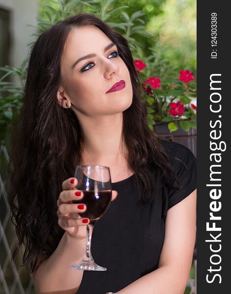 Young beautiful girl holding glass with red wine and relaxing in garden