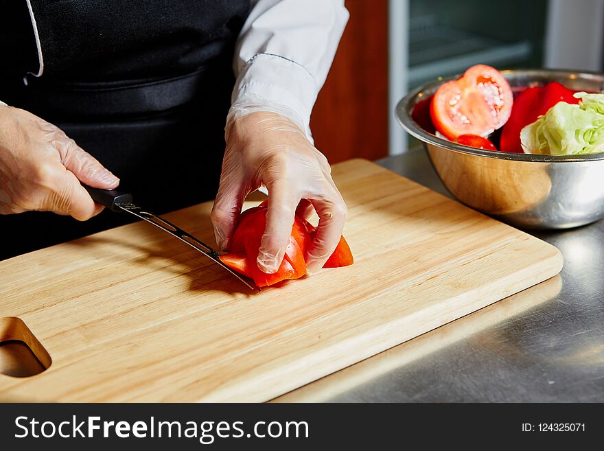 The chef in the cafe cuts tomatoes on a wooden kitchen Board.