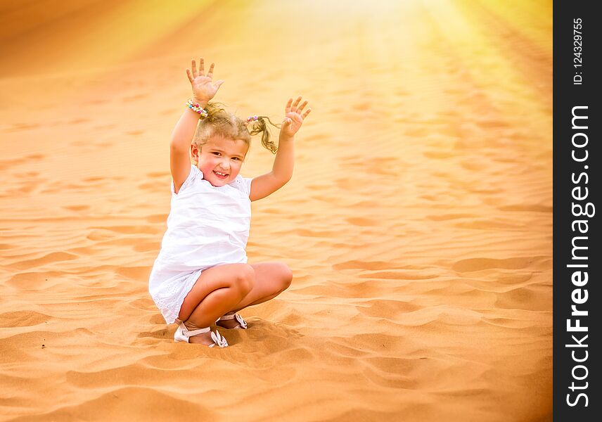 Little girl smiles and plays sand in the desert.