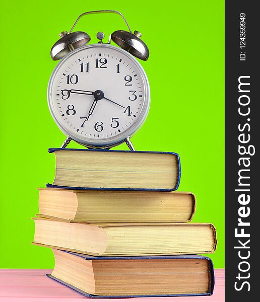 Alarm clock on top of piles of books on yellow background.