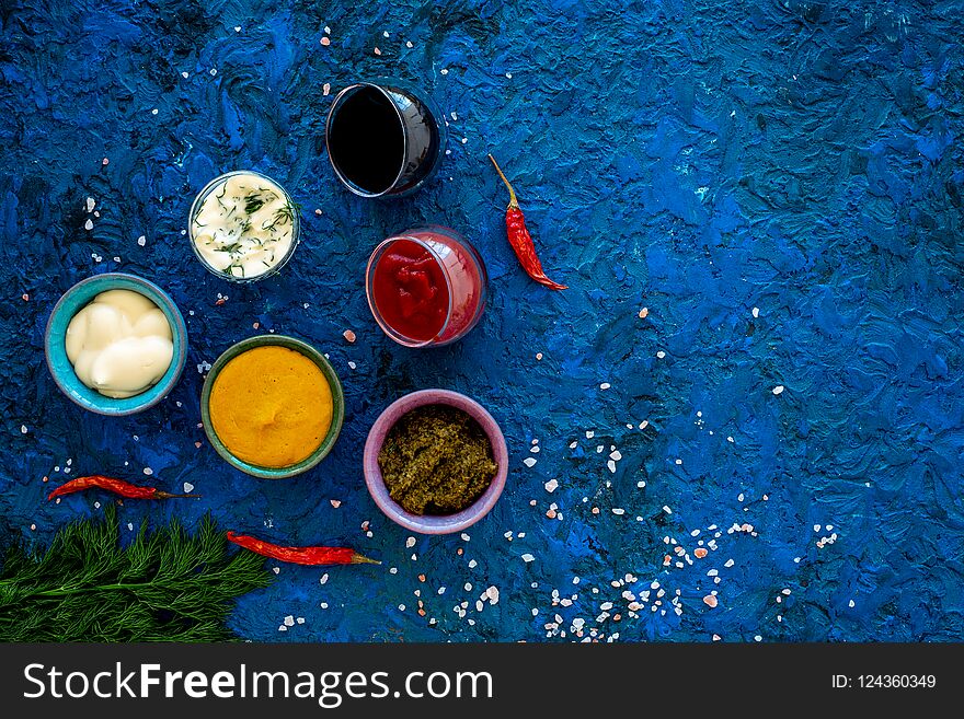 Spicy sauses. Ketchup, mayonnaise, mustard, soy sauce, barbecue sauce, pesto, mustard, sour near chili pepper and greenery on blue background top view.