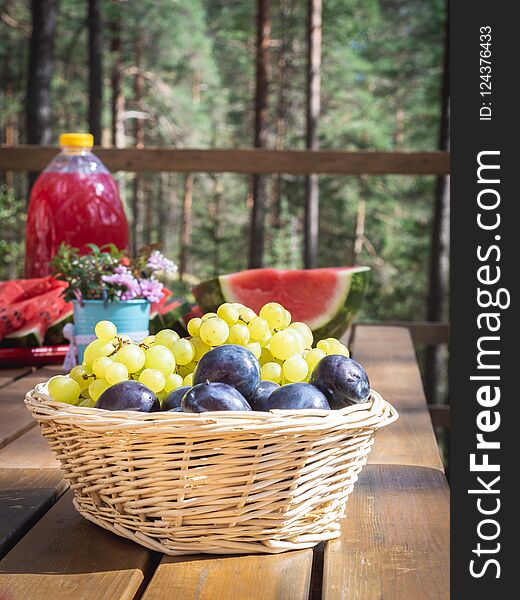Closeup of basket with grapes and plumps on a wooden table, outdoor party or picnic