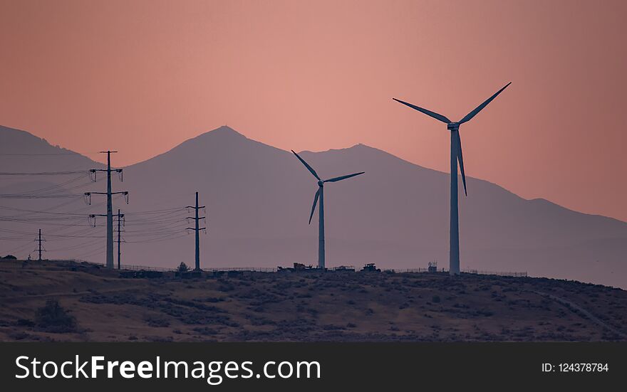 Large ind turbines generating electricity in the sunset wind and the mountains in the background. Large ind turbines generating electricity in the sunset wind and the mountains in the background