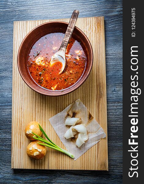 top view on wooden plate with traditional ukrainian borscht next to baked doughnut with garlic topping decorated with green onion and sliced tallow. top view on wooden plate with traditional ukrainian borscht next to baked doughnut with garlic topping decorated with green onion and sliced tallow