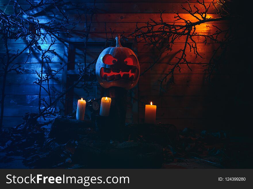 Concept of Halloween. glowing orange and blue light with angry terrible pumpkin, leaves, jack-lamp with candle of a happy Halloween, on a wooden background