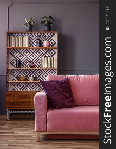 Red pillow on pink couch in retro living room interior with wooden cabinet. Real photo