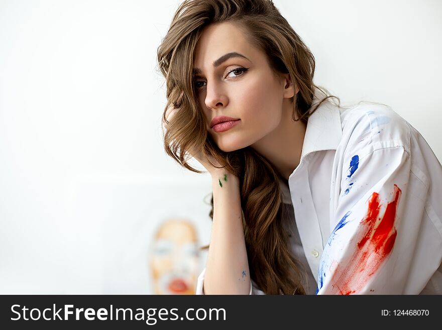 Young beautiful woman portrait on white stained with paint shirt. Thoughtful artist in studio