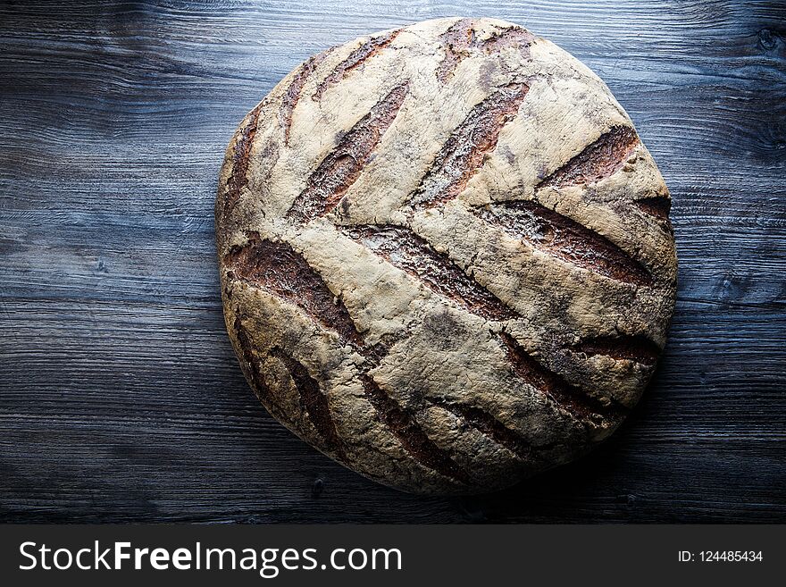 big whole handmade round black bread with interesting texture lie on dark wooden table