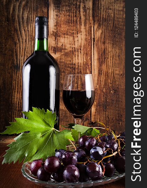 Red grape on plate with vine decoration and glass and bottle of red wine