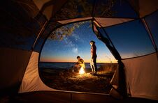 Young Couple Man And Woman Having Rest At Tourist Tent And Burning Campfire On Sea Shore Near Forest Royalty Free Stock Image