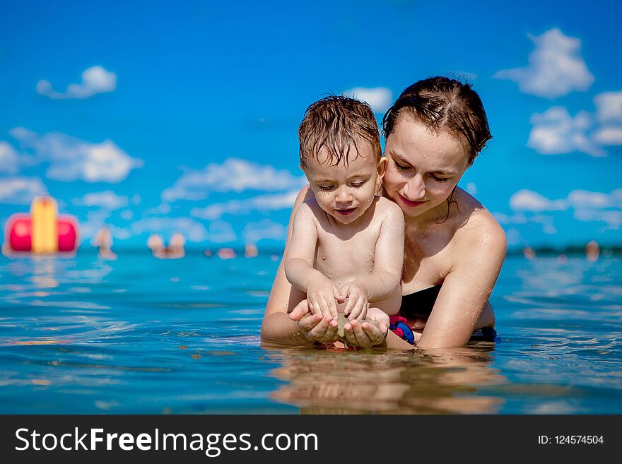 Young mother with a little boy playing with water on the lake in the summer, family happiness, country family rest, summer warm day, happiness.