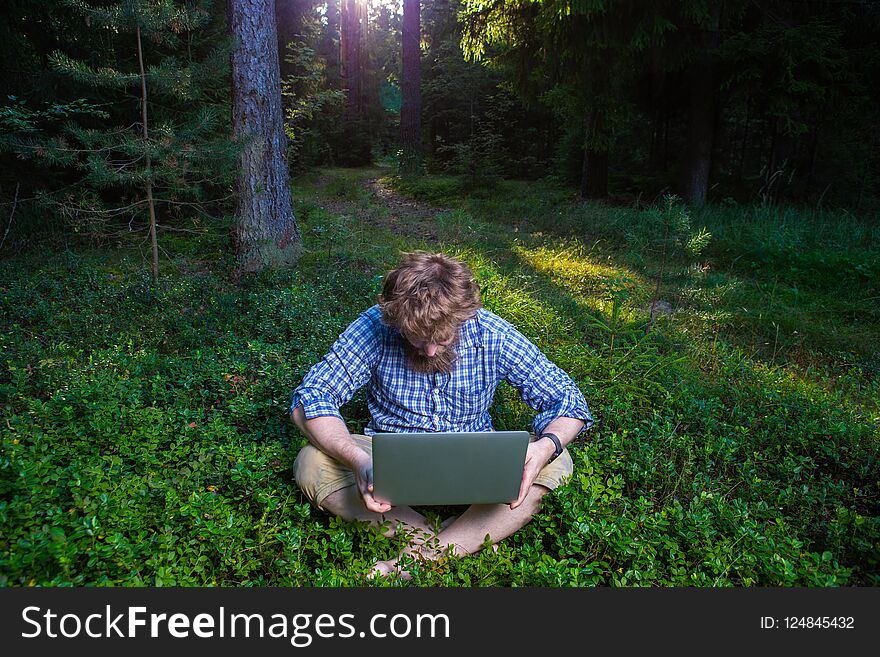 Shot of confused and surprised Caucasian bearded hipster feeling frustrated, sitting at outdoor in the wood with generic laptop pc, trying to concentrate on work, looking exhausted. Shot of confused and surprised Caucasian bearded hipster feeling frustrated, sitting at outdoor in the wood with generic laptop pc, trying to concentrate on work, looking exhausted.