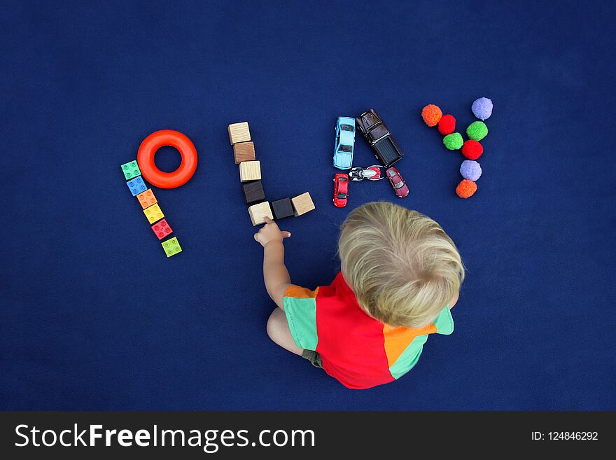 Little blond boy with inscription PLAY made from different toys on blue textile background. Childhood concept. Good for baby store.