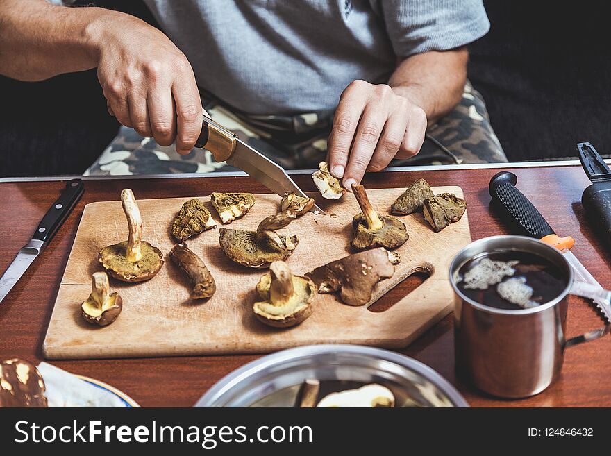 Processing of collected mushrooms. Hands of a man cut fresh edible porcini mushrooms on a wooden board. Processing of collected mushrooms. Hands of a man cut fresh edible porcini mushrooms on a wooden board