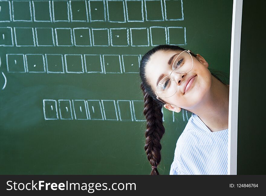 Student in glasses stays near blackboard in classroom