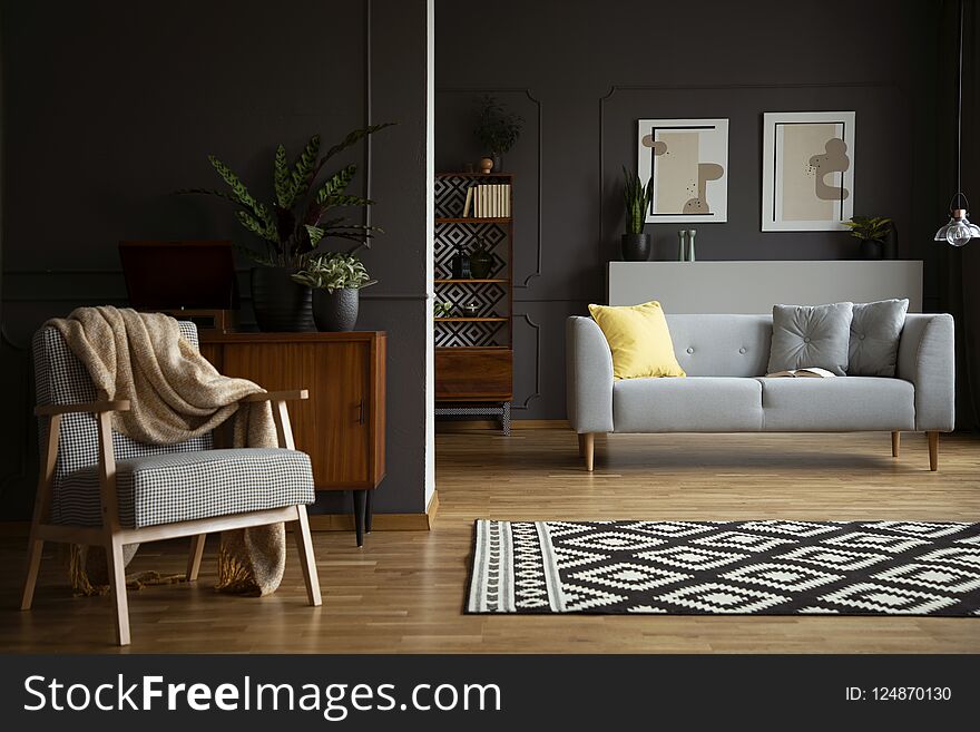 Blanket on armchair next to patterned carpet in living room interior with grey sofa. Real photo
