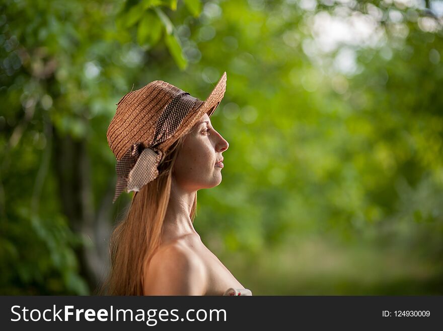 Portrait of a beautiful elegant woman in light white dress and hat standing in the summer park.