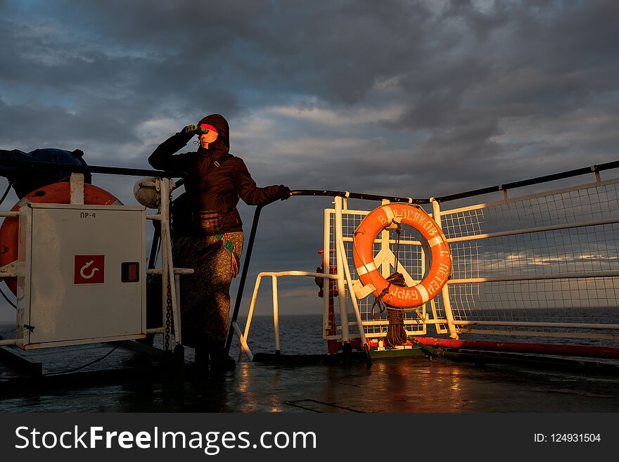 A girl on a ship looks through binoculars at sunset