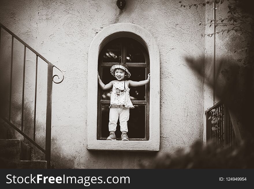 Black and white of Happy cute little girl smiling and standing by the window with vintage color tone.