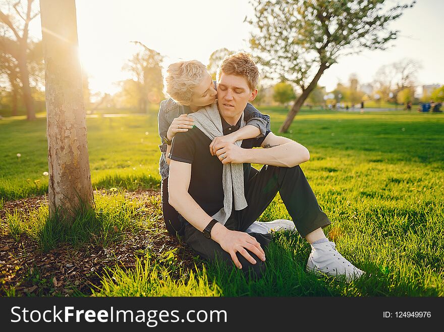 Stylish and beautiful women with short light hair, dressed in a blue jeans jacket sitting with her handsome men in a sunny green park. Stylish and beautiful women with short light hair, dressed in a blue jeans jacket sitting with her handsome men in a sunny green park