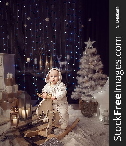 A little boy in a white jumpsuit sitting on a white toy moose. The concept of Christmas. A little boy in a white jumpsuit sitting on a white toy moose. The concept of Christmas