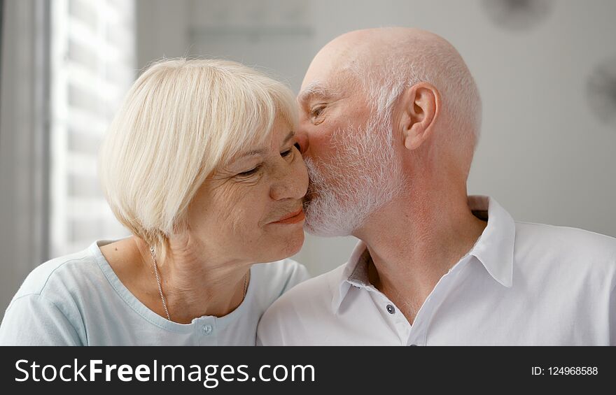 Portrait of happy senior couple at home. Senior man expresses his emotions and kisses his wife