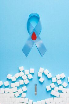 Blue Ribbon Awareness With Red Blood Drop And Wall Made Of Sugar Cubes Ruined By Glucose Test Strips On Blue Background Stock Image
